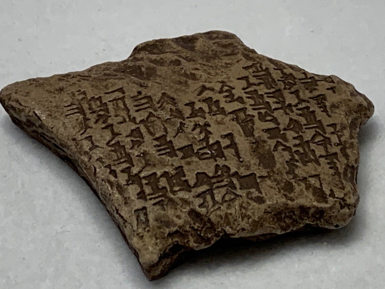 May include: A brown clay tablet with cuneiform script. The tablet is rectangular with rounded edges and has a rough texture. The script is carved into the surface of the tablet.