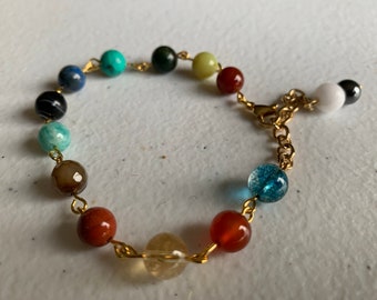 May include: A gold chain bracelet with a variety of colored beads, including red, green, blue, and brown. The bracelet has a clasp closure.