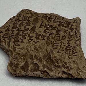 May include: A close-up of a small, brown, irregularly shaped stone with cuneiform script carved into its surface.
