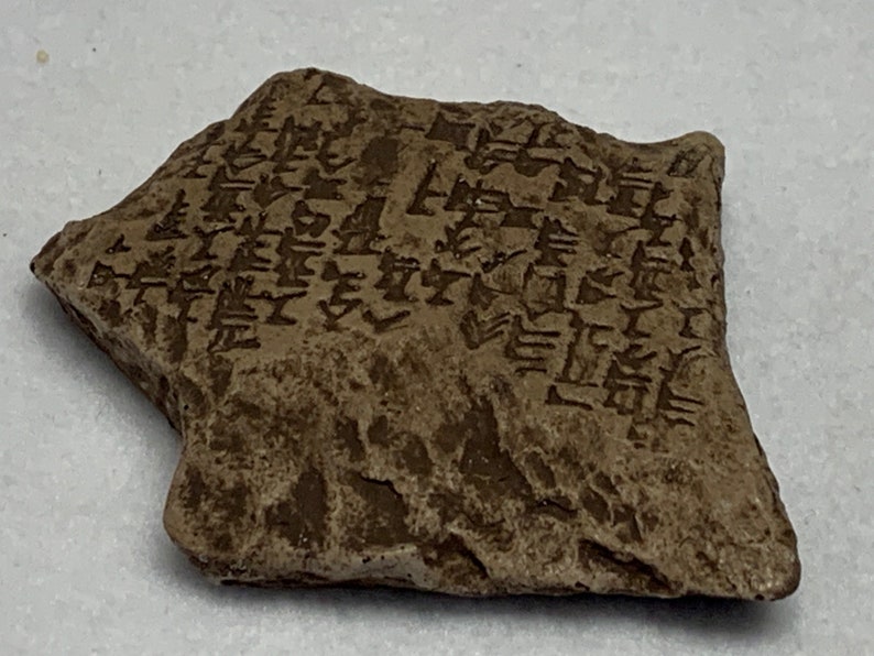 May include: A close-up of a small, brown, irregularly shaped stone with cuneiform script carved into its surface.