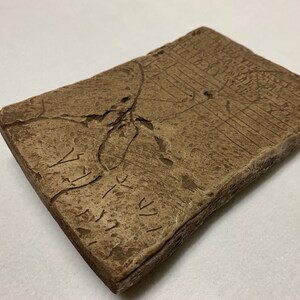 May include: A brown rectangular stone tablet with ancient cuneiform script carved into its surface. The tablet has several cracks and chips.