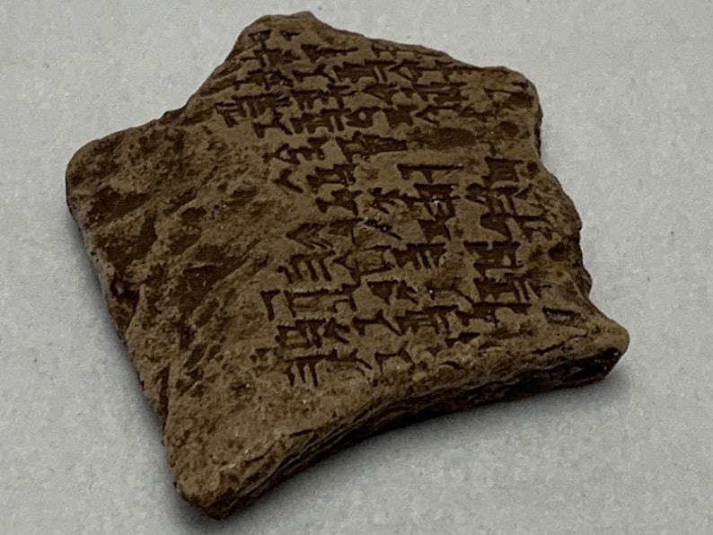 May include: A brown clay tablet with cuneiform script, an ancient form of writing used in Mesopotamia.