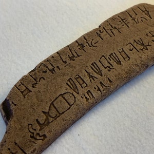 May include: A close-up of a brown stone tablet with ancient writing carved into its surface. The writing is in a script that is difficult to decipher, but it appears to be a form of ancient writing.