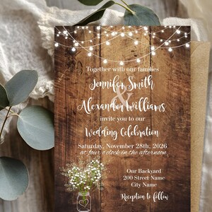 May include: A rectangular wedding invitation card featuring a dark brown wood grain background, white string lights at the top, and a mason jar with baby's breath at the bottom. The text reads: Together with our families, Jennifer Smith & Alexander Williams invite you to our Wedding Celebration, Saturday, November 28th, 2026 at four o'clock in the afternoon, Our Backyard, 200 Street Name, City Name, Reception to follow.