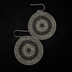 May include: A pair of silver earrings with a circular design. The earrings are made of a chainmail-like material and have a black and silver color scheme.