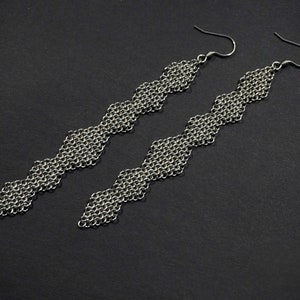 May include: A pair of long silver earrings with a geometric diamond pattern.