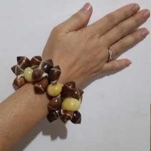 May include: A bracelet made of brown and yellow seashells. The bracelet is made of many small shells that are strung together.