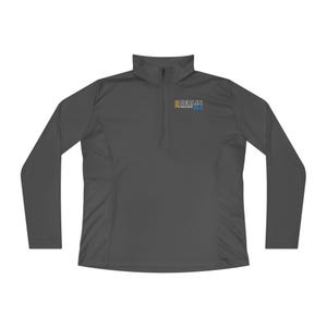 May include: A dark gray long-sleeve quarter-zip pullover featuring a high collar and a small graphic on the left chest. The graphic includes the text 2023 BERLIN FINISHER 26.2 in yellow, white, and blue lettering against the dark gray fabric.