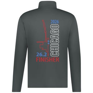 May include: A dark gray long-sleeve quarter-zip pullover featuring a graphic on the back. The design includes a red outline of a map, two blue stars, the text "CHICAGO 2026" in white, and the blue text "26.2" above the red text "FINISHER".