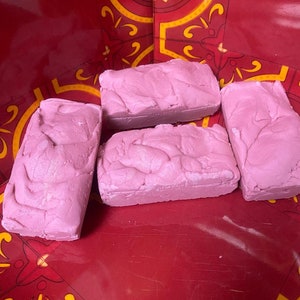 May include: Four pink bars of soap on a red background with a yellow and gold pattern. The soap is textured and has a slightly marbled appearance.