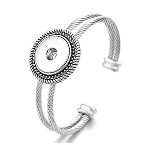 May include: Silver bangle bracelet with a decorative round snap button charm. The bracelet is made of twisted metal.