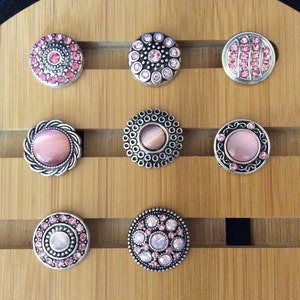 May include: Nine round pink and silver snap buttons with various designs.