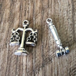 May include: Two silver charms, one shaped like a scale of justice and the other shaped like a gavel.