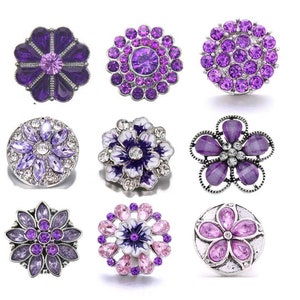 May include: Nine purple and white flower-shaped snap buttons with rhinestones. The buttons are silver-toned and have a variety of designs.