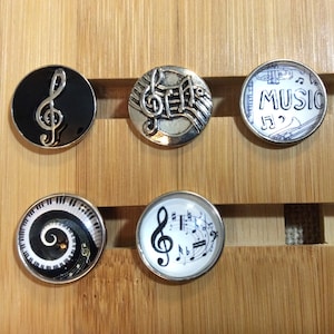 May include: Six round, silver-rimmed, decorative buttons with various music-themed designs. The designs include a treble clef, musical notes, a piano keyboard, and the word "MUSIC".