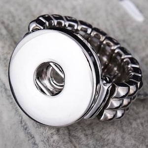 May include: A silver adjustable ring with a large, round, white button-like charm. The ring is made of multiple linked bands.