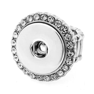 May include: A silver ring with a large, round, white button-like center surrounded by a row of clear rhinestones.
