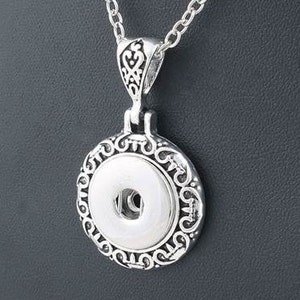 May include: Silver necklace with a round pendant featuring an ornate design and a white button in the center.