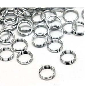 May include: A large quantity of silver-toned metal jump rings. The rings are all the same size and are arranged in a random pattern.