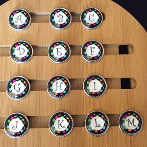 May include: A set of 14 round, black and silver snap charms with colorful polka dots and white letters A through M.