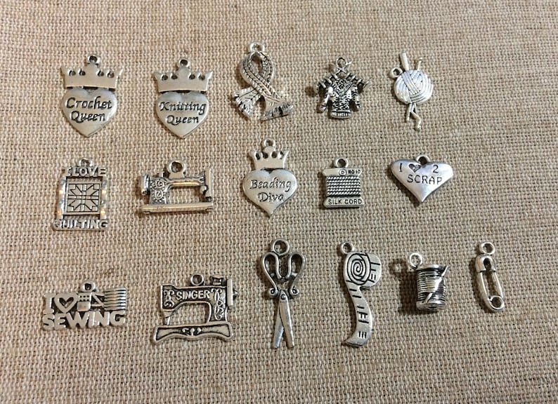 Puede incluir: Una colecci&oacute;n de 15 dijes de metal plateados con varios temas de costura y manualidades. Los dijes presentan im&aacute;genes de m&aacute;quinas de coser, tijeras, carretes de hilo, cinta m&eacute;trica y otros suministros de manualidades. Algunos dijes tienen texto en ellos, como "Crochet Queen", "Knitting Queen", "Beading Diva", "I Love Quilting", "I Love Sewing" y "1 2 Scrap".