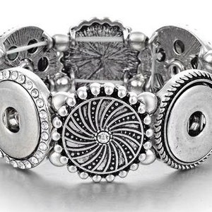 May include: Silver bracelet with two large snap buttons and a decorative swirl design. The bracelet is made of metal and has a beaded design.