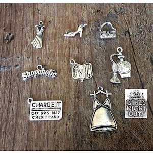 May include: A set of silver charm pendants with various designs, including a dress, a shoe, a purse, a perfume bottle, a credit card, a book, a dress, and a sign that says "Girls Night Out!"