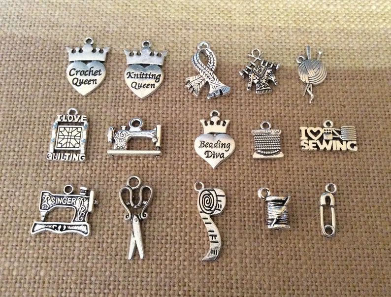 Puede incluir: Una colecci&oacute;n de 15 abalorios de metal plateados con varios temas de costura y artesan&iacute;a. Los abalorios presentan im&aacute;genes de m&aacute;quinas de coser, tijeras, carretes de hilo, agujas, lana y m&aacute;s. Algunos abalorios tienen texto, como "Crochet Queen", "Knitting Queen", "Beading Diva", "I Love Quilting" y "I Love Sewing".