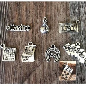 May include: A collection of silver charm pendants with casino and gambling themes. The charms include a bag of money, a horseshoe, a dice, a bingo card, a lottery ticket, a deck of cards, and a $100 bill.