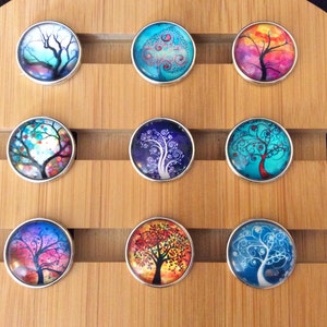 May include: Nine round, silver-rimmed, glass cabochons with colorful tree designs. Each cabochon features a different tree design with various colors, including blue, green, red, orange, and purple.