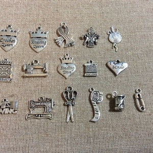 Puede incluir: Una colecci&oacute;n de 15 colgantes de amuleto de plata con varios temas de artesan&iacute;a, que incluyen costura, tejido, ganchillo, acolchado y abalorios. Los amuletos son todos en forma de corazones, coronas u otras herramientas de artesan&iacute;a.