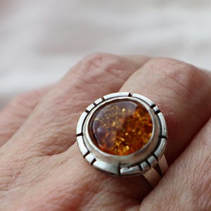 May include: A silver ring with a round amber stone set in a textured bezel. The ring has a simple band.