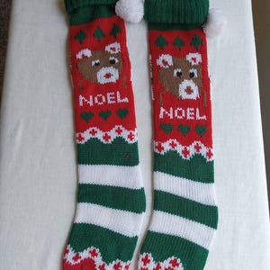 May include: Two red and green Christmas stockings with a reindeer design and the word "NOEL". The stockings have white and green stripes at the bottom and a white pom-pom at the top. A festive holiday decoration.