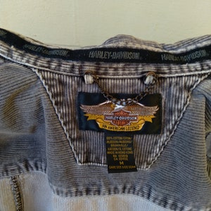 May include: A gray corduroy jacket with a Harley-Davidson logo patch. The patch is embroidered with the Harley-Davidson logo and the words "An American Legend". The jacket has a size tag that says "M".