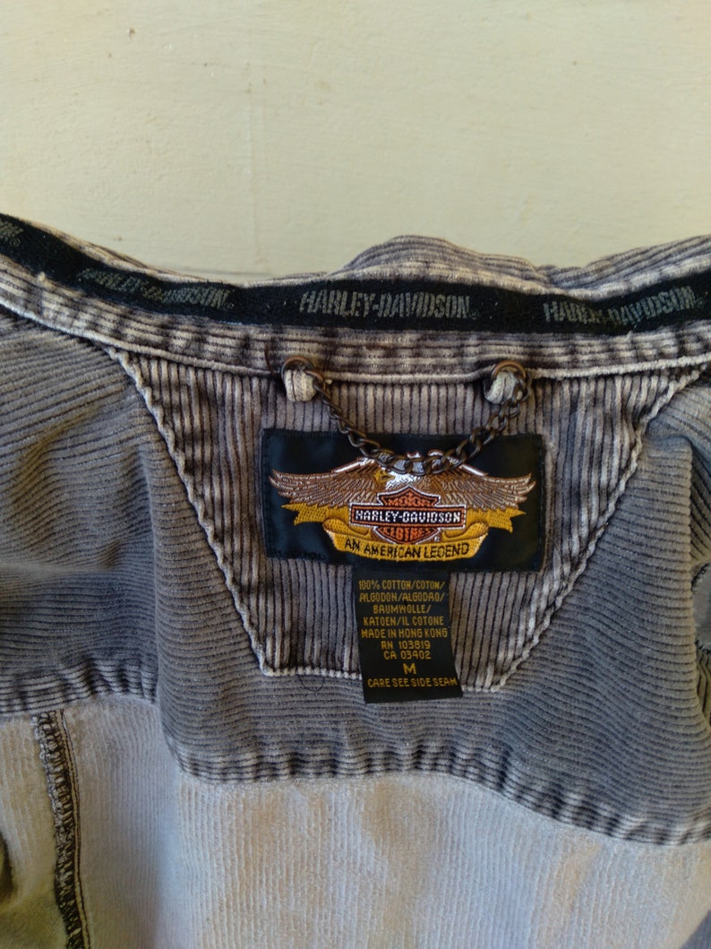May include: A gray corduroy jacket with a Harley-Davidson logo patch. The patch is embroidered with the Harley-Davidson logo and the words "An American Legend". The jacket has a size tag that says "M".