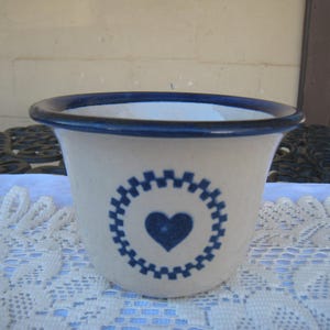May include: A white ceramic bowl with a blue rim and a blue heart design. The bowl has a scalloped edge and a blue and white pattern around the heart.