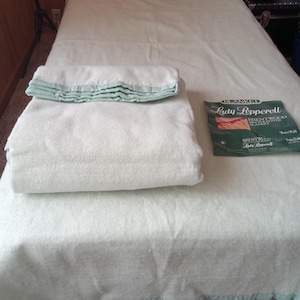 May include: A light green twin-size blanket with a matching folded blanket and a package labeled "Lady Pepperell". The blanket has a ruffled edge in a lighter shade of green.