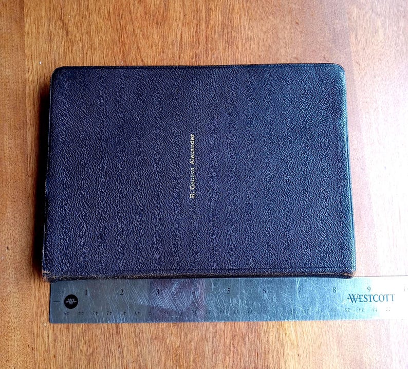 May include: A rectangular, dark purple, textured book cover with the name R. Geneva Alexander embossed in gold lettering. A metal Westcott ruler is positioned along the bottom edge, showing the book is approximately 9 inches in length.