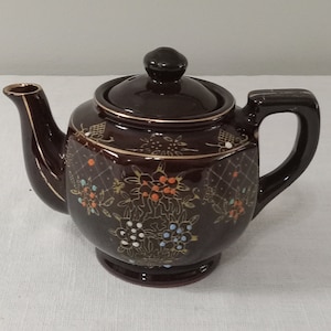 May include: A brown teapot with a gold and floral design. The teapot has a lid and a handle.
