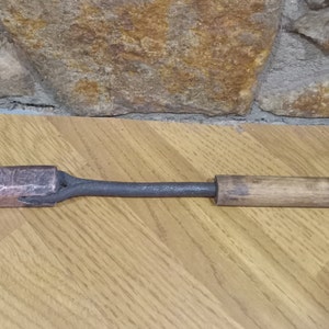 May include: A vintage soldering iron with a wooden handle and a copper tip. The iron is made of metal and has a dark gray finish.