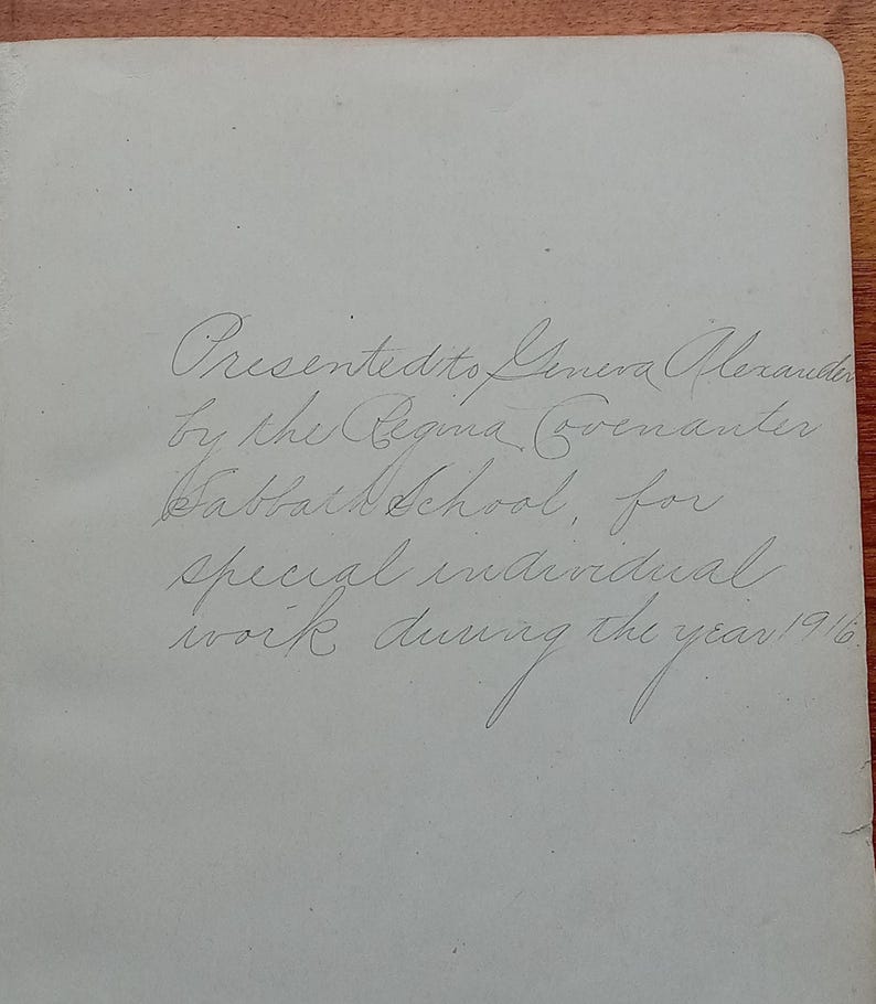 May include: A light-colored page from a book featuring handwritten cursive text that reads: Presented to Geneva Alexander by the Regina Covenanter Sabbath School, for special individual work during the year 1916.