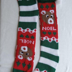 May include: Two knitted Christmas stockings. One is red with a reindeer design and the word "NOEL". The other is red, green, and white striped. Both have green cuffs and white pom-poms.
