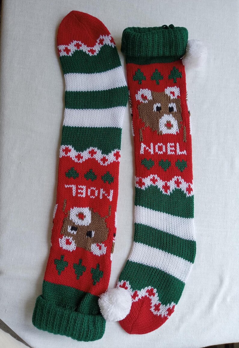 May include: Two knitted Christmas stockings. One is red with a reindeer design and the word "NOEL". The other is red, green, and white striped. Both have green cuffs and white pom-poms.