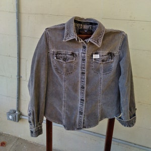 May include: A gray corduroy button-up shirt with a long sleeve and two chest pockets. The shirt has a small white label with the text "Barneys New York" on the front.