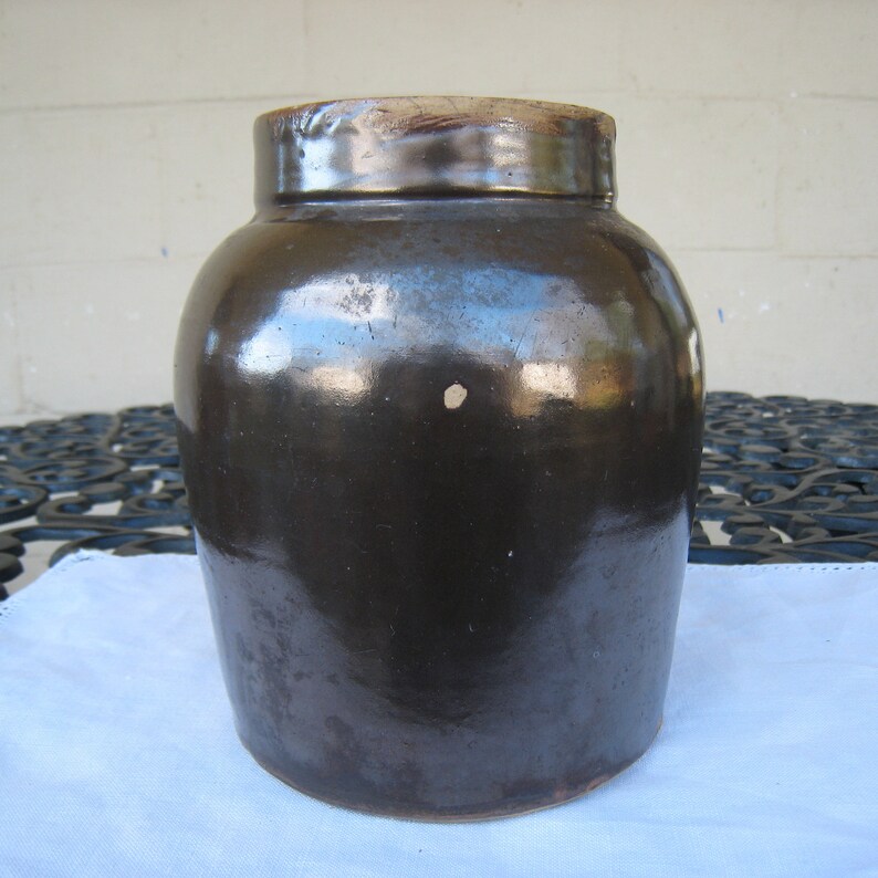 May include: A dark brown glazed ceramic crock with a rounded body and a wide mouth.