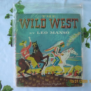 May include: A vintage children's book cover with a colorful illustration of a cowboy on a brown horse and an Native American on a white horse. The book title is "The Wild West" by Leo Manso. The book is a Rainbow Playbook.