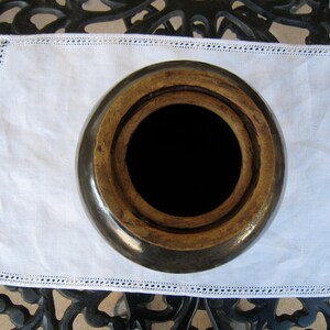 May include: A brown ceramic crock with a wide opening and a wooden lid. The crock is sitting on a white doily with lace trim.