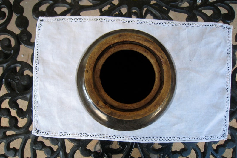 May include: A brown ceramic crock with a wide opening and a wooden lid. The crock is sitting on a white doily with lace trim.