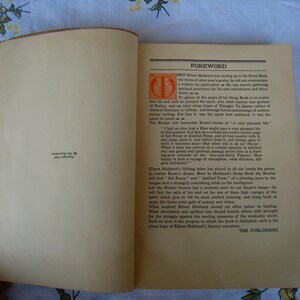 May include: An open vintage book with cream-colored pages. The right page features a foreword titled in black text with an orange decorative initial letter. The left page contains small black text near the bottom reading Copyright, 1923, By The Roycrofters.