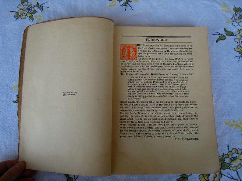 May include: An open vintage book with cream-colored pages. The right page features a foreword titled in black text with an orange decorative initial letter. The left page contains small black text near the bottom reading Copyright, 1923, By The Roycrofters.